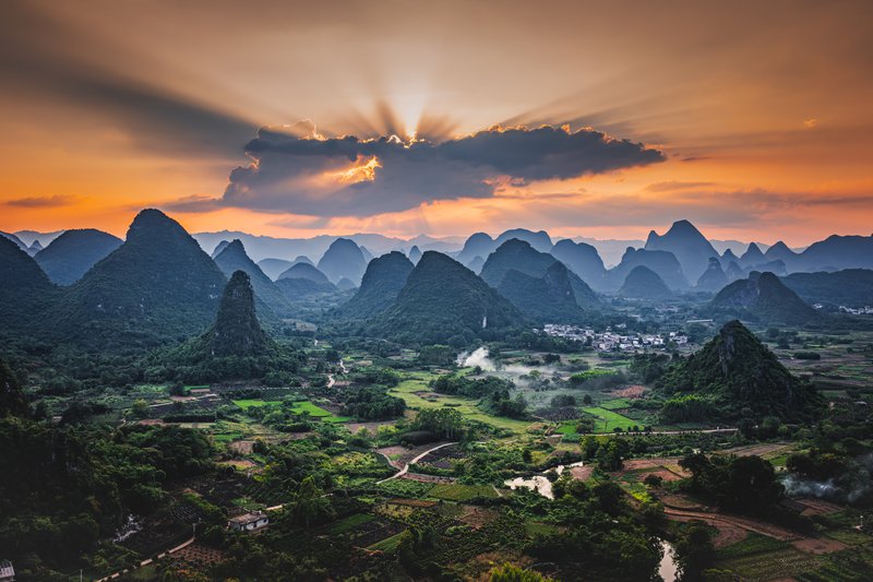 Sunburst through clouds over karst landscape