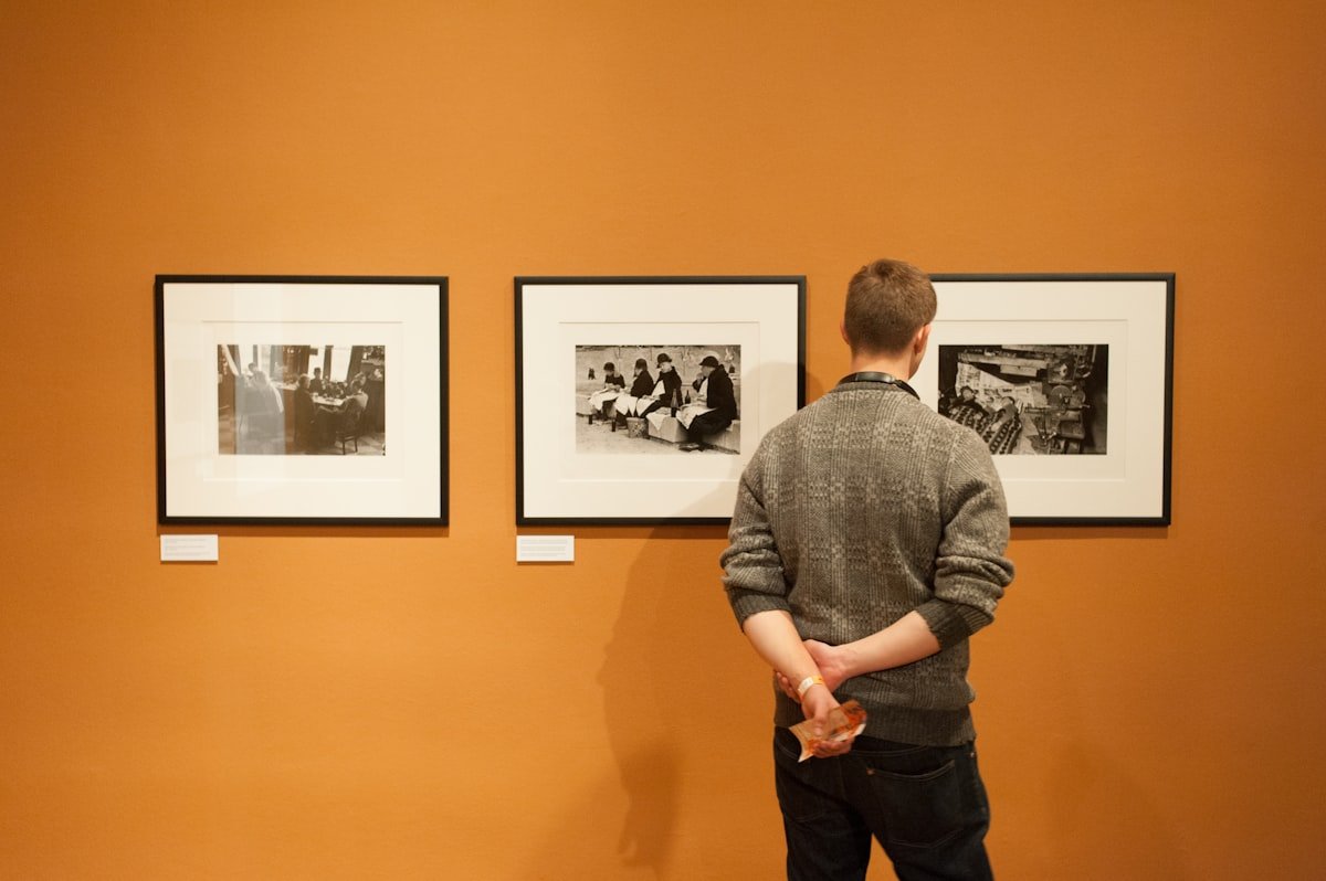 Person viewing framed black and white photography prints hung on a gallery wall with professional museum lighting