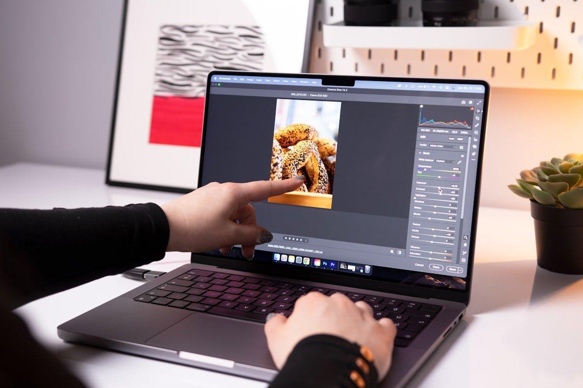 Photographer editing photos on a modern MacBook Pro laptop with photo editing software interface visible on screen
