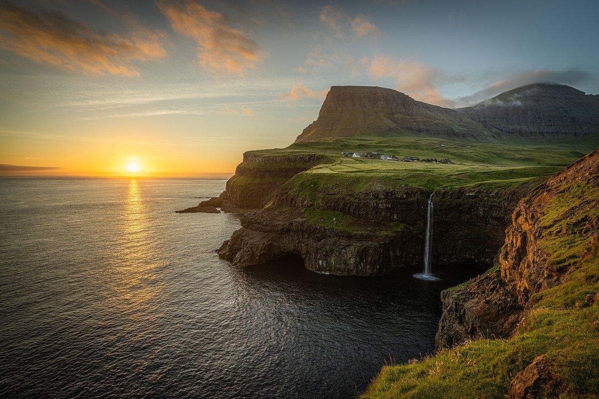 Aerial view of Mulafossur waterfall plunging from green sea cliffs into the North Atlantic Ocean at Gasadalur village in the Faroe Islands