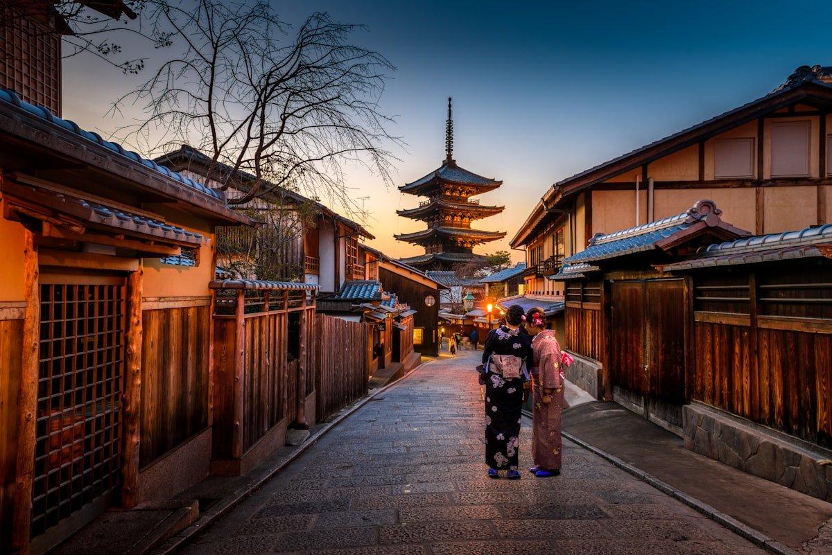 Traditional Japanese temple with cherry blossom trees in full bloom reflected in a garden pond at golden hour