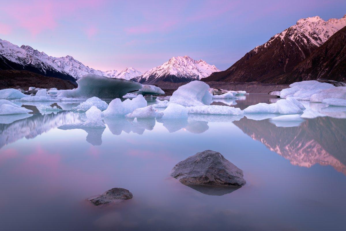 Aoraki Mount Cook at sunrise with pink alpenglow reflected perfectly in a still glacial lake in New Zealand South Island
