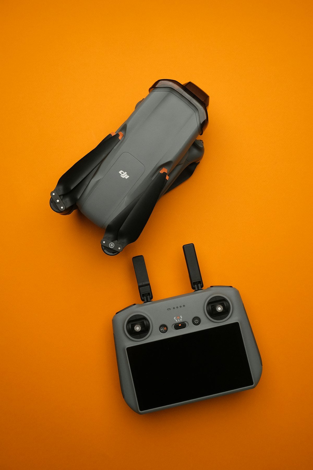 Modern DJI drone folded with remote controller on vibrant orange background, ready for international travel photography