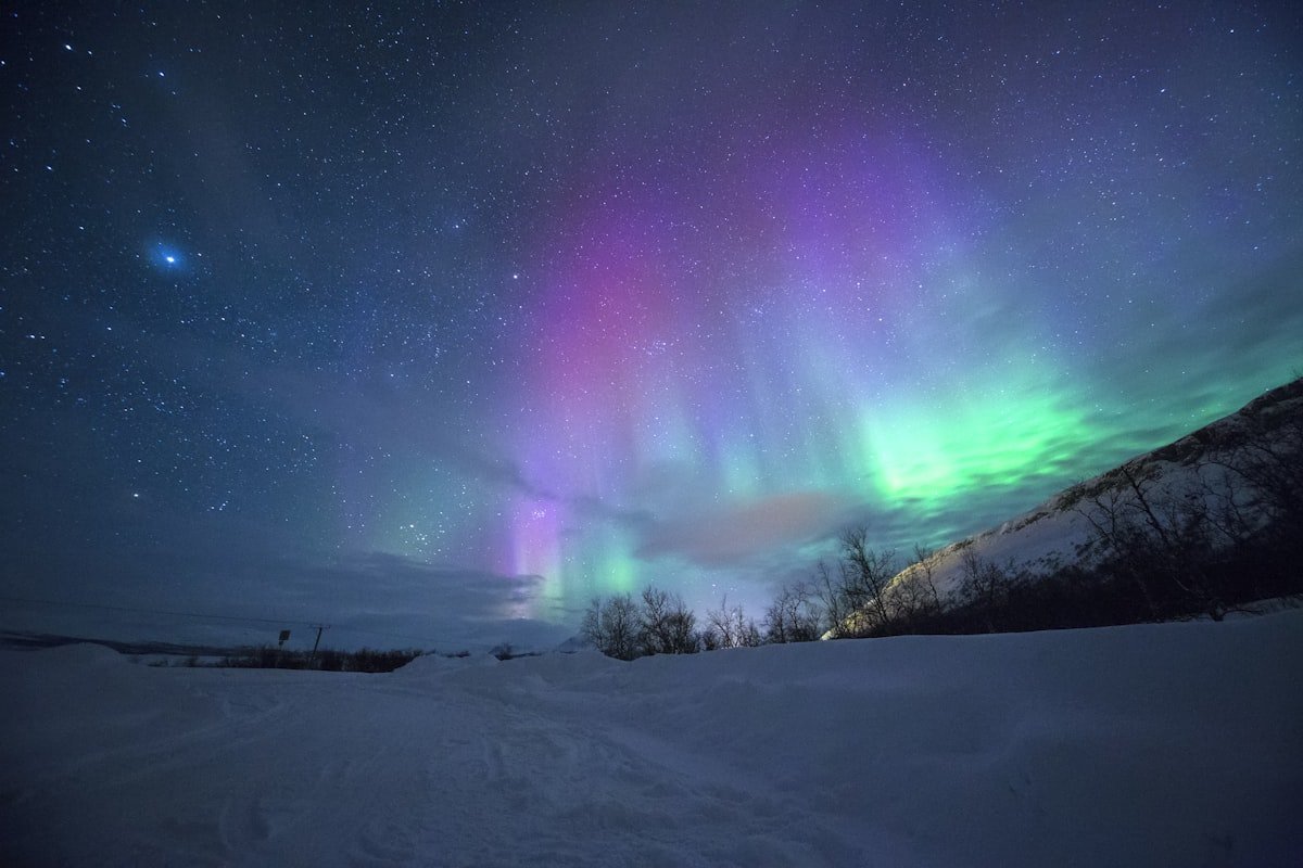 Vibrant green aurora borealis over snowy Icelandic mountains reflected in still water
