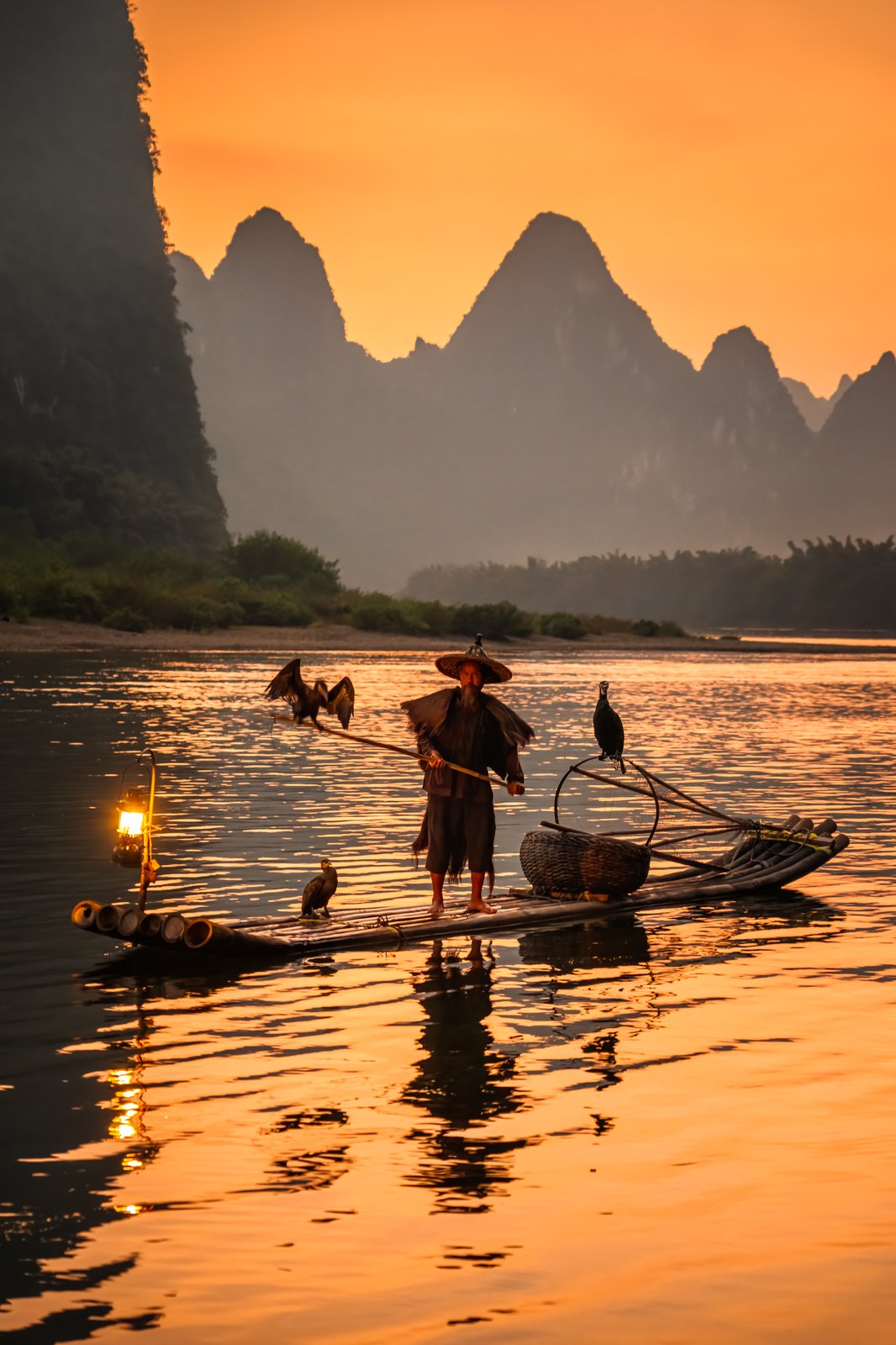 Traditional cormorant fisherman at golden hour on the Li River, karst peaks behind
