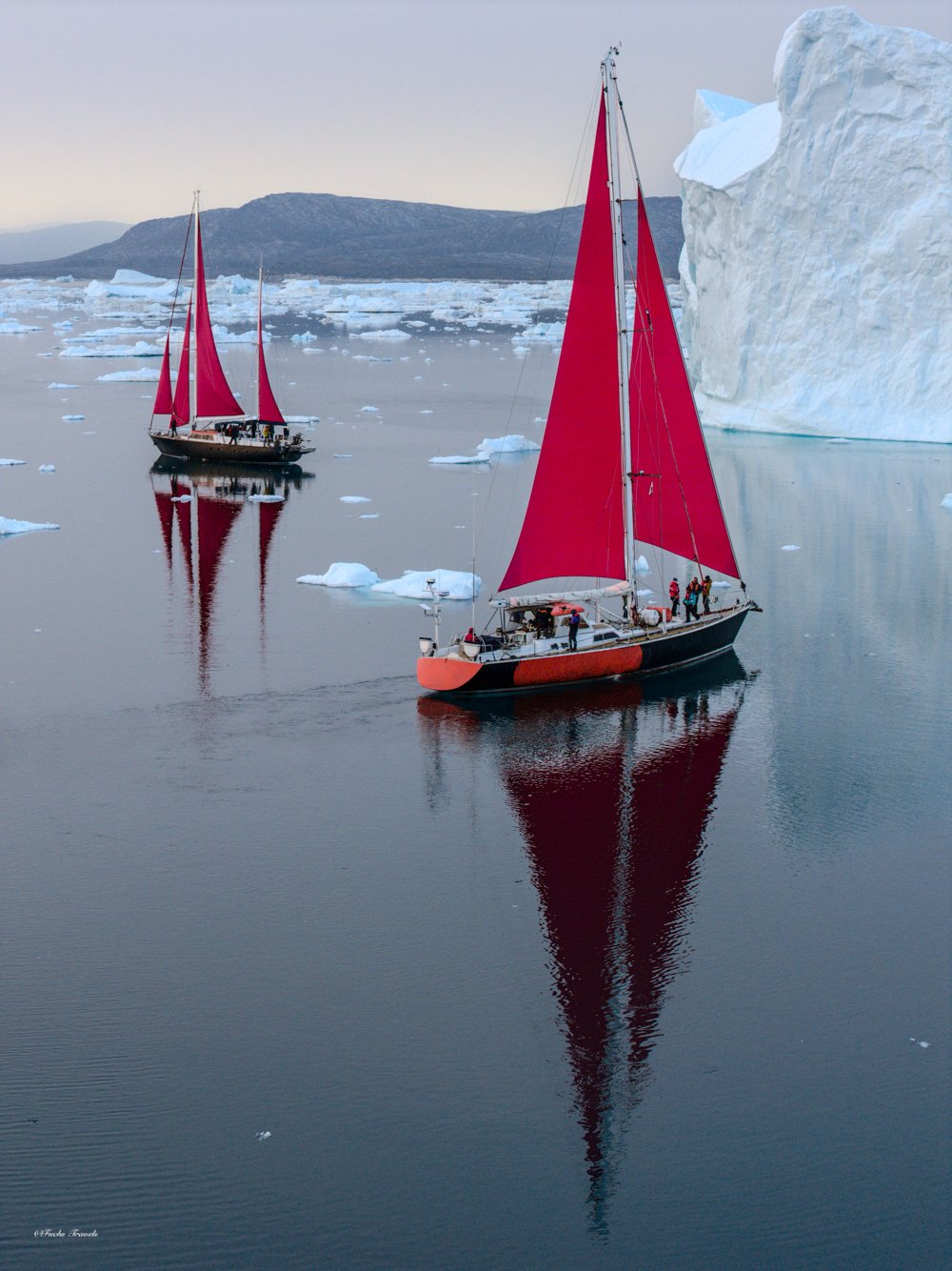 Two red-sailed boats perfectly reflected in the still waters among icebergs, captured from an aerial drone perspective