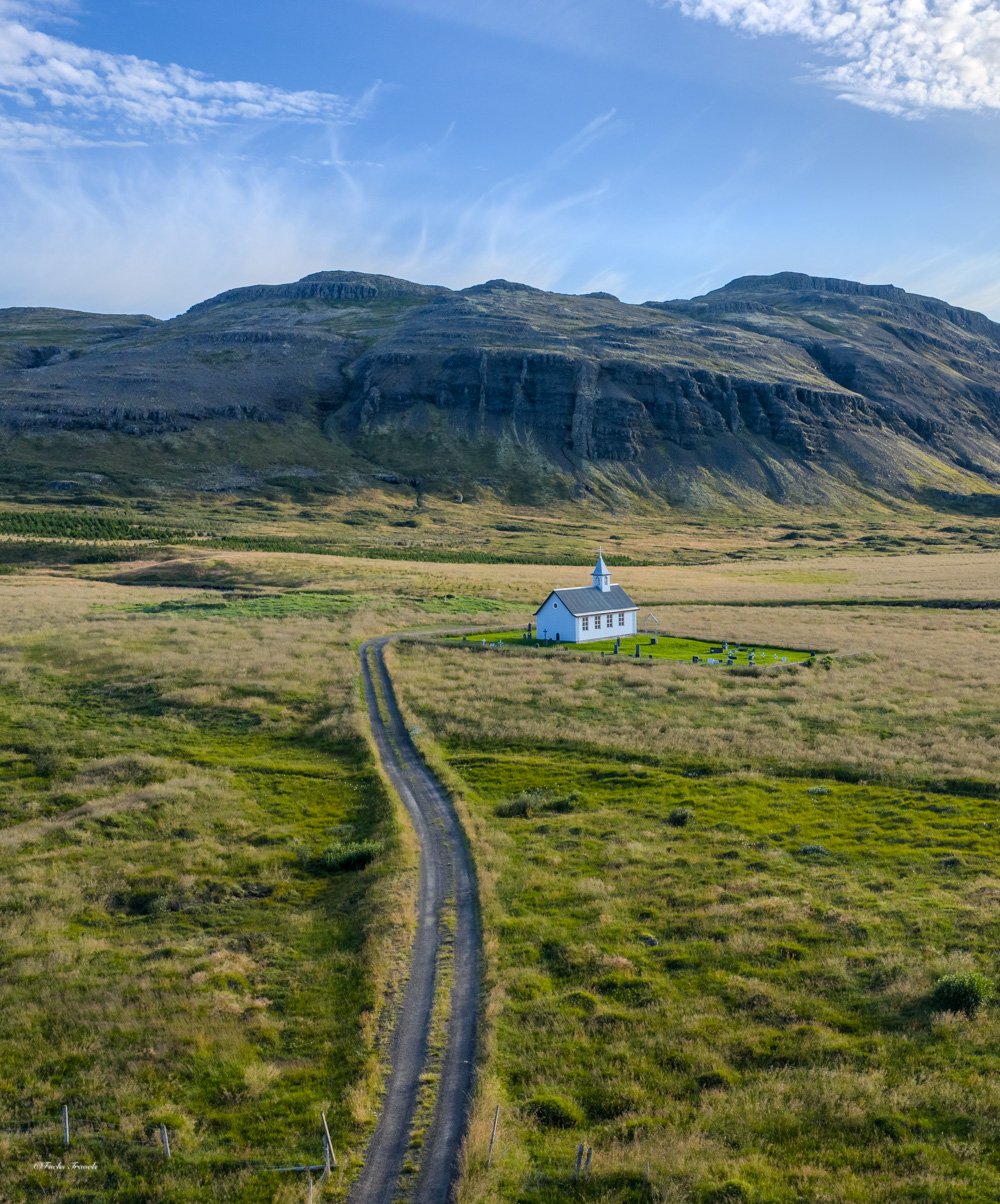 Lonely Icelandic church at the end of a winding dirt road with layered mountains in summer light