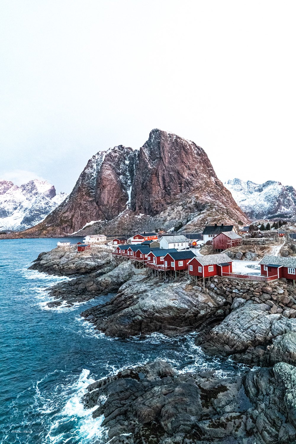 The iconic red rorbu cabins of Hamnoy perched on rocky shores with dramatic mountain peaks rising behind