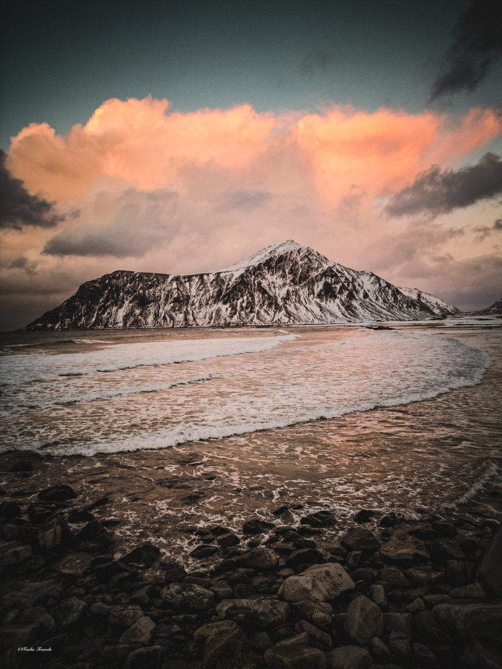 Pink sunset clouds over snow-capped Lofoten mountain reflected in wet sand at Skagsanden Beach