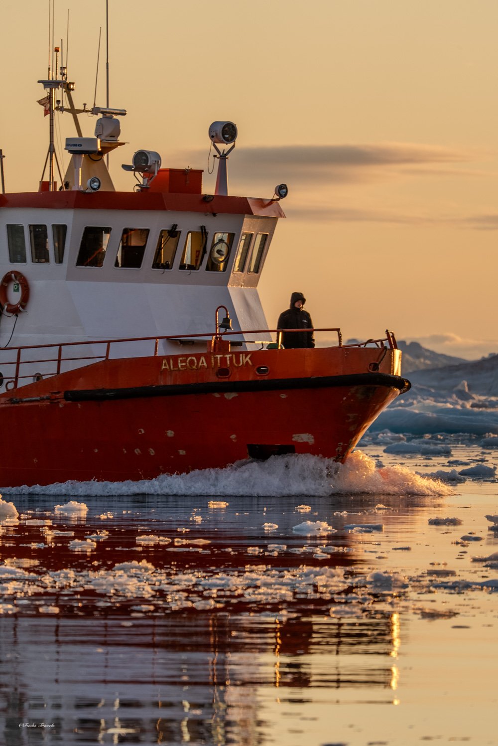 The Aleqa Ittuk expedition vessel moving through ice-filled waters of Disko Bay at golden hour