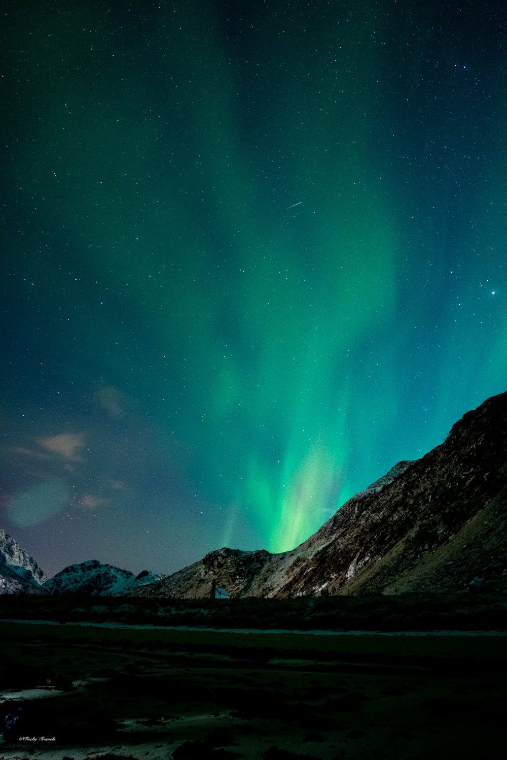 Vivid green aurora curtains rising from behind Lofoten mountain peaks under a star-filled sky
