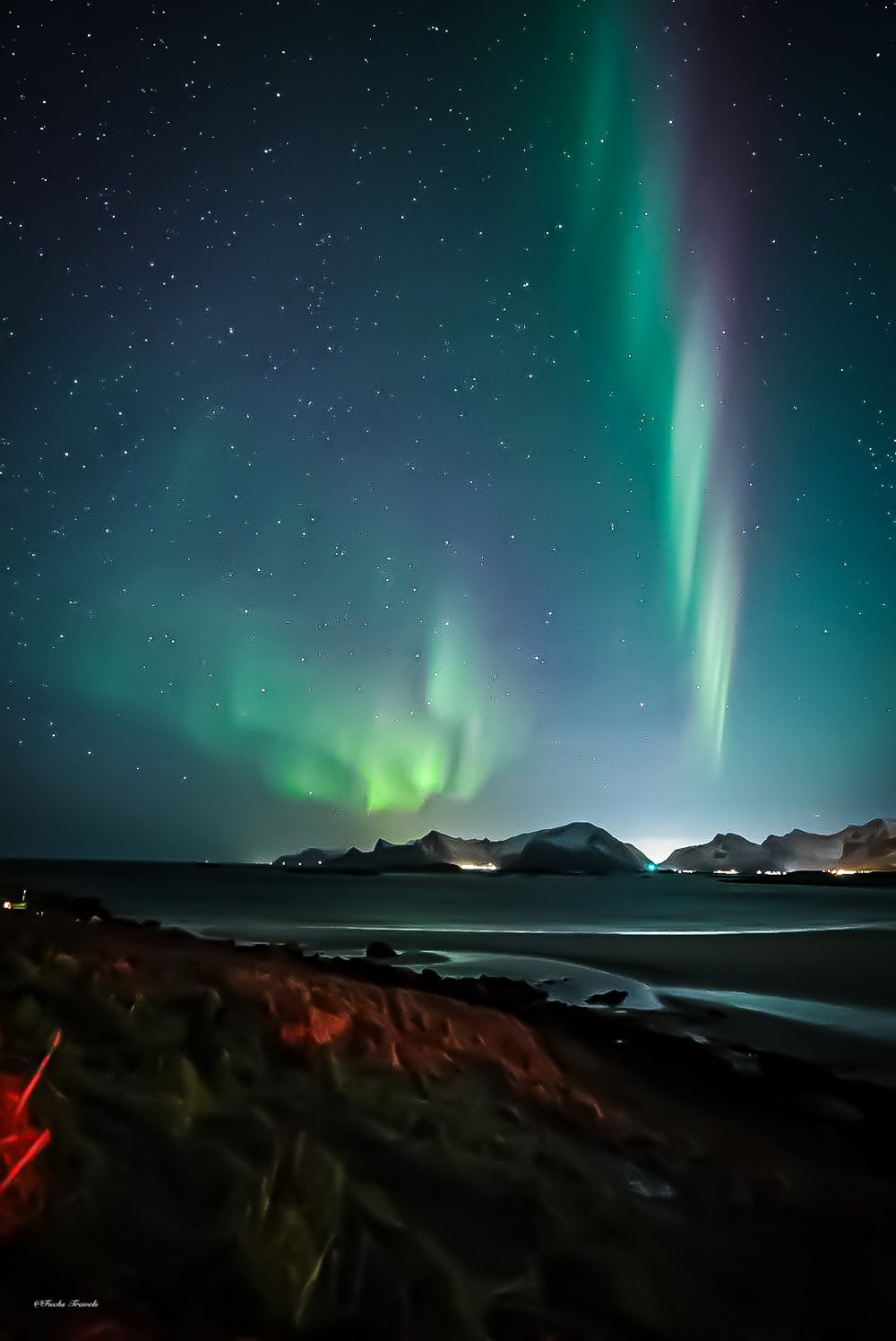 Aurora borealis with stars and purple bands stretching across the arctic sky over a Lofoten beach