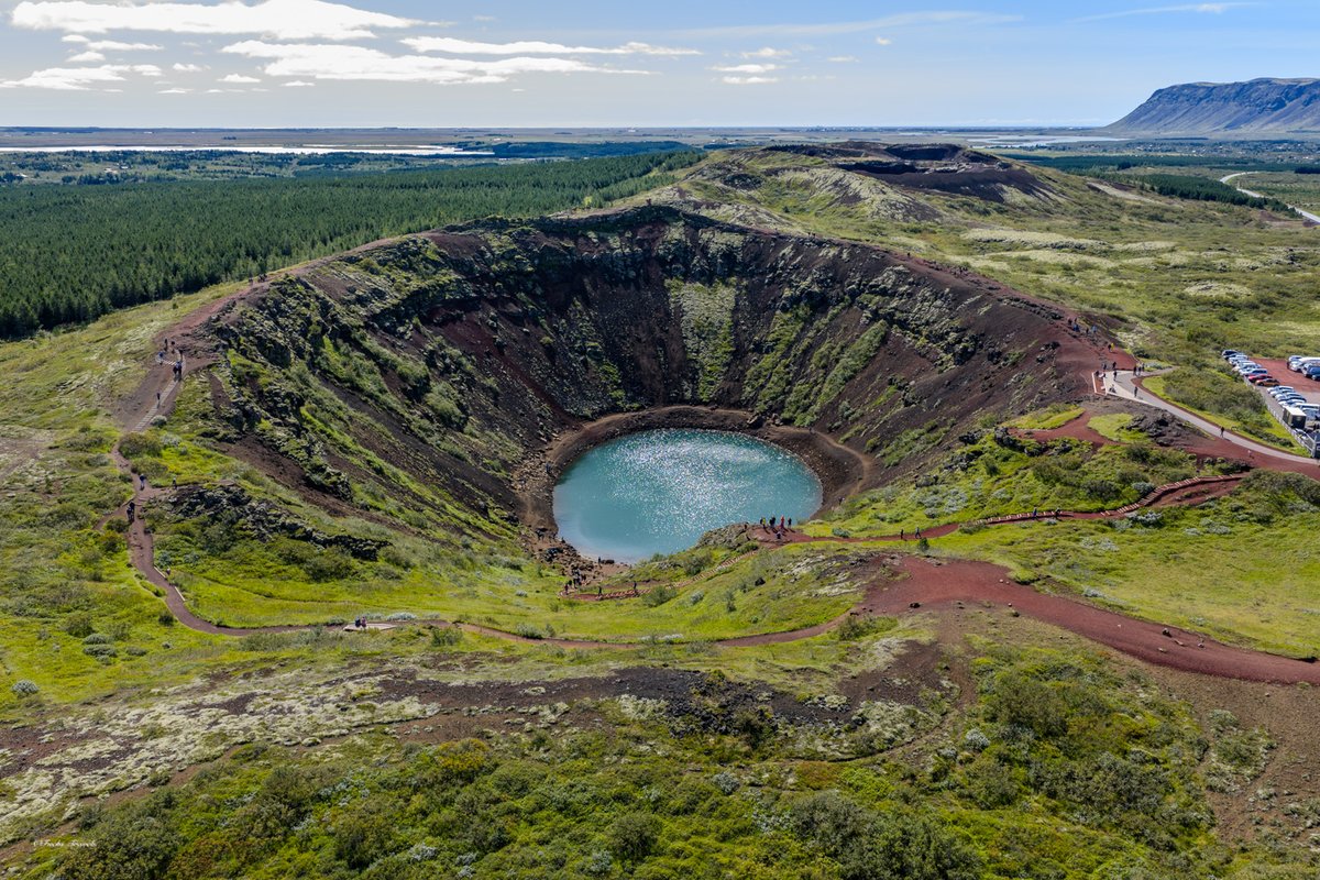 Kerið volcanic crater with turquoise lake seen from drone altitude, vivid green moss surrounding the rim
