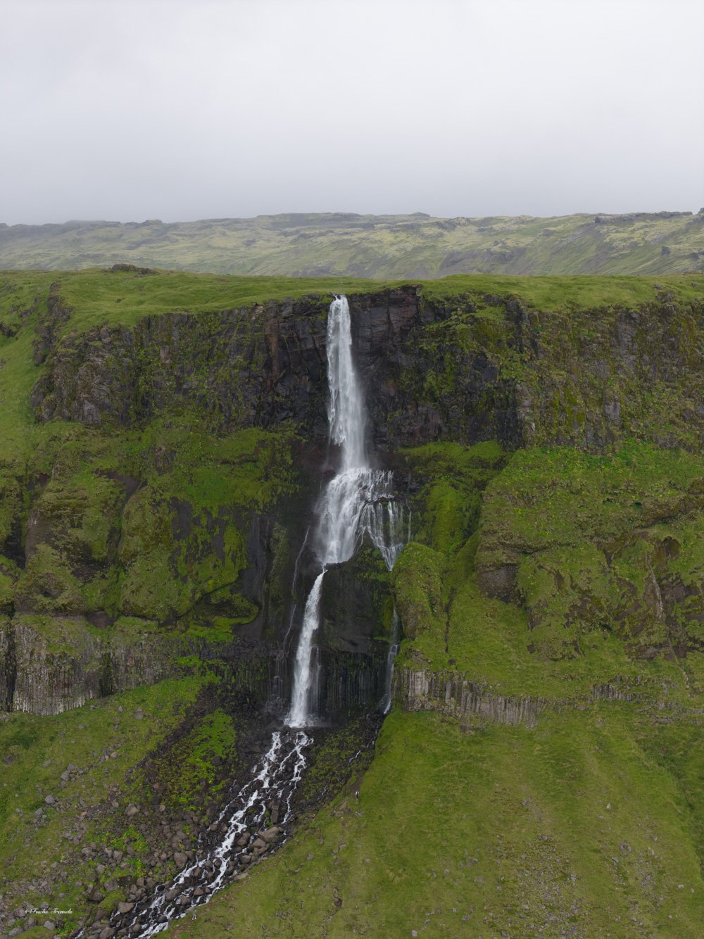 Multi-tiered Icelandic waterfall cascading over green moss-covered basalt cliffs, captured from drone
