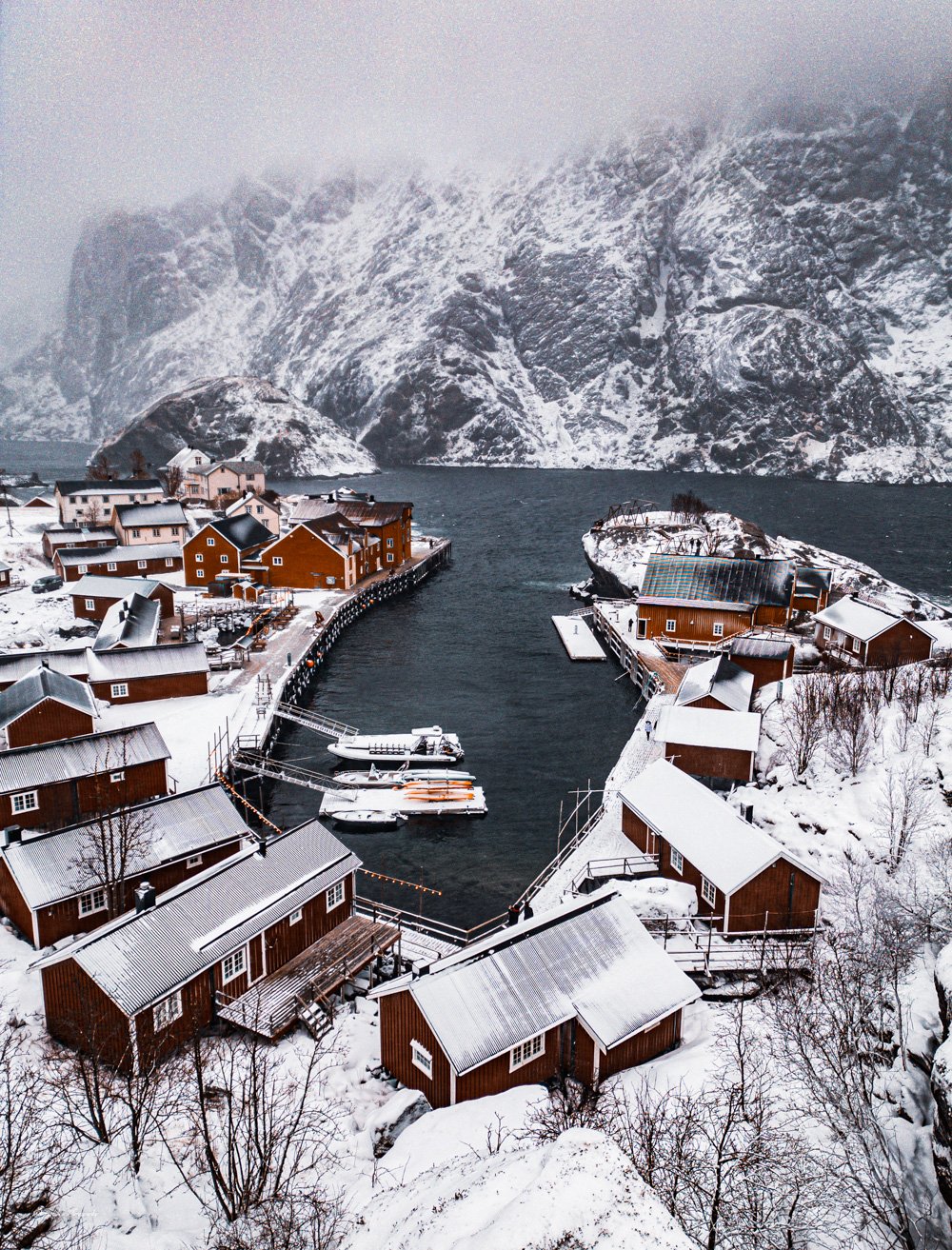 Drone aerial of the historic fishing village of Nusfjord in Norway's Lofoten Islands, showing red rorbu cabins along the fjord